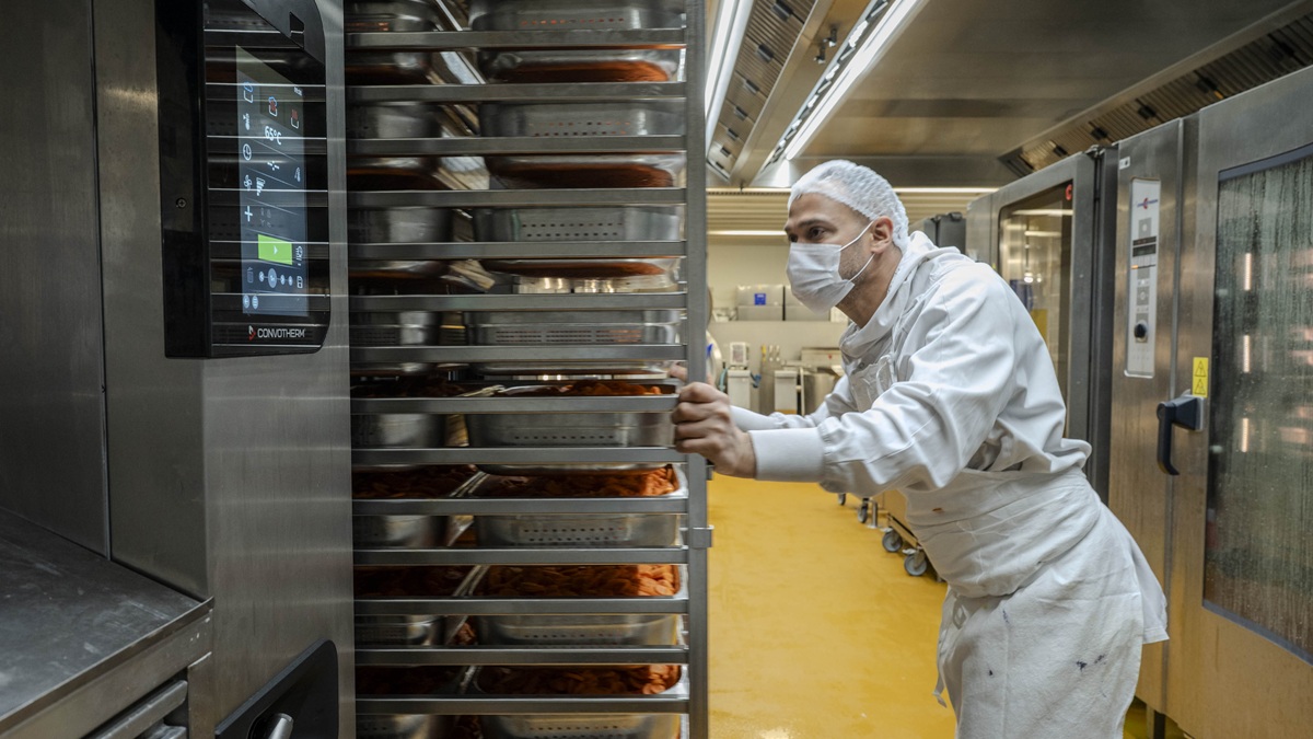 Un agent de cantine entrepose des bacs de nourriture pour la cuisson