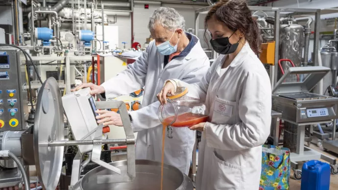 Deux personnes versent un liquide dans une cuve, dans une halle technologique agroalimentaire